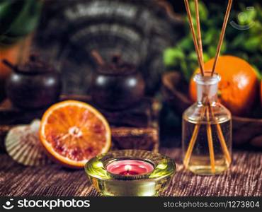 Aromatherapy composition with candle, citrus fruit, aromatherapy bottle with wooden sticks.