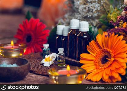 Aromatherapy composition with transparent aromatherapy bottles filled with blue and green essential oils, colorful red and orange flowers, red candles, sea salt in wooden bowl and small white flowers decor background. Aromatherapy relax concept.