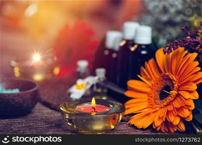 Aromatherapy composition with transparent aromatherapy bottles filled with blue and green essential oils, colorful red and orange flowers, red candles, sea salt in wooden bowl and small white flowers decor background. Aromatherapy relax concept.