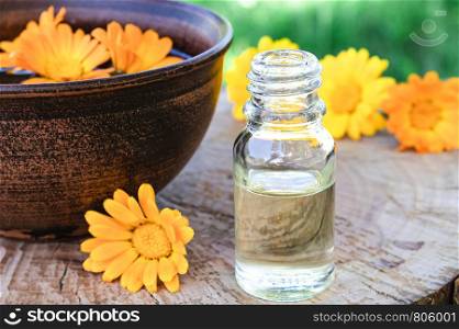 Aromatherapy essential oil with calendula flowers on a wooden background in nature. Extract of calendula tincture in a bowl. Medicinal plants.. Aromatherapy essential oil with calendula flowers on a wooden background in nature. Extract of calendula tincture in a bowl.