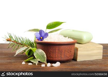 Aromatic bath salt in a clay cup, soap and green leaves on a wooden background
