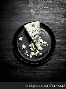 Aromatic cheese with blue mold on an old plate. On a black wooden background.. Aromatic cheese with blue mold on an old plate.