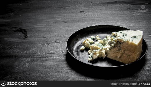 Aromatic cheese with blue mold on an old plate. On a black wooden background.. Aromatic cheese with blue mold on an old plate.