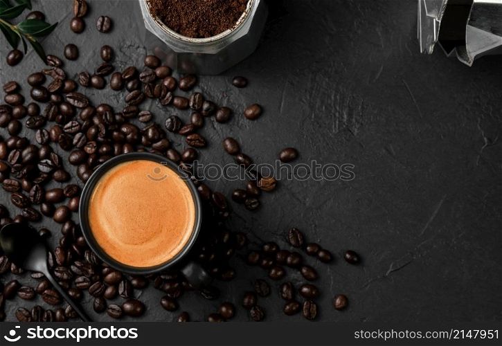 Aromatic espresso coffee in a cup on a black table next to a coffee pot. Coffee beans and coffee ingredients on the table. Top view, place for text. Italian style breakfast idea.