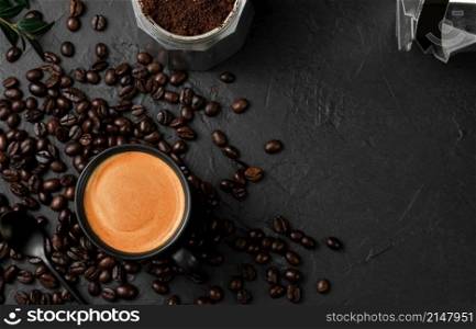 Aromatic espresso coffee in a cup on a black table next to a coffee pot. Coffee beans and coffee ingredients on the table. Top view, place for text. Italian style breakfast idea.