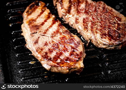 Aromatic grilled steak in a frying pan. Against a dark background. High quality photo. Aromatic grilled steak in a frying pan.