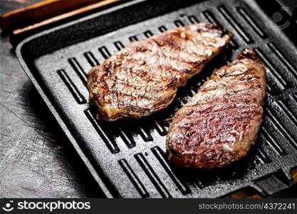 Aromatic grilled steak in a frying pan. Against a dark background. High quality photo. Aromatic grilled steak in a frying pan.