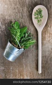 aromatic herbs in metal pot and wooden spoon on board
