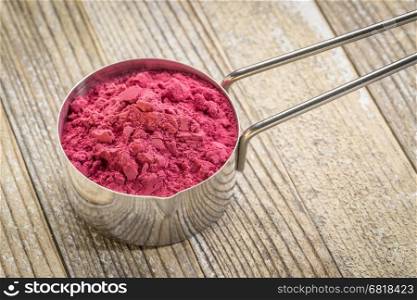 aronia berry (chokeberry) powder in a metal measuring scoop against grunge wood background