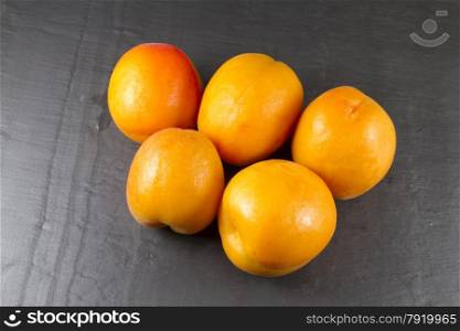 Arrangement of five apricots on a slate background.