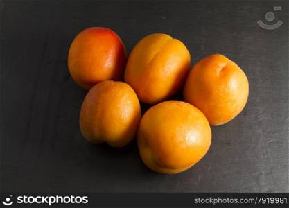 Arrangement of five apricots on a slate background.
