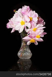 Arrangement of Peony blossoms in a cut glass vase reflecting off table and isolated against black