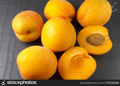 Arrangement of six apricots on a slate background, one halved with stone.