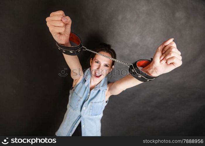 Arrest and jail. Criminal angry woman prisoner girl showing leather handcuffs on gray. Punishment.