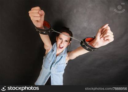 Arrest and jail. Criminal angry woman prisoner girl showing leather handcuffs on gray. Punishment.