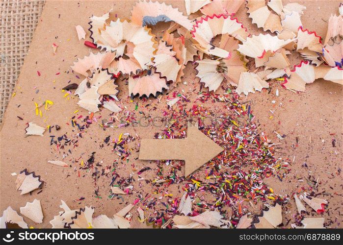 Arrow cut out of paper amid pencil shavings on canvas