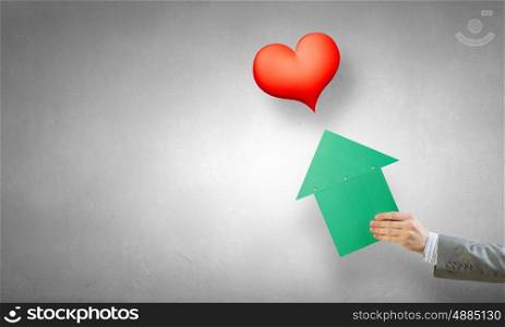 Arrow pointer in hand. Person hand pointing with green arrow at red heart