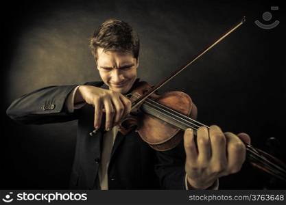Art and artist. Young elegant emotional man violinist fiddler playing violin on dark gray. Classical music. Studio shot.