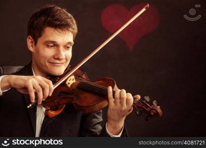 Art and artist. Young elegant in love man violinist fiddler playing violin on black background with valentine heart love symbol. Classical music. Studio shot.