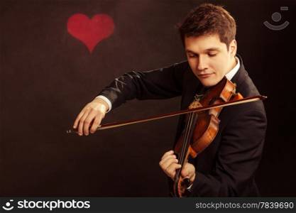 Art and artist. Young elegant in love man violinist fiddler playing violin on black background with valentine heart love symbol. Classical music. Studio shot.