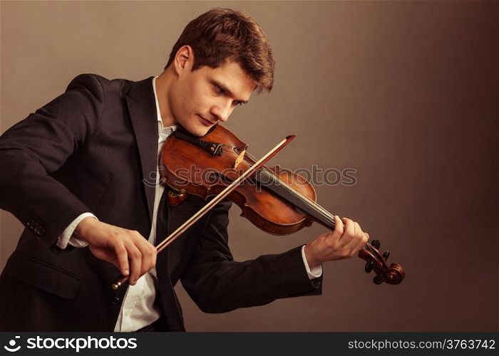 Art and artist. Young elegant man violinist fiddler playing violin on brown. Classical music. Studio shot.