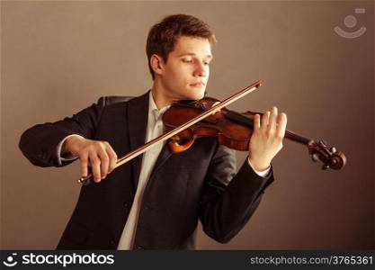 Art and artist. Young elegant man violinist fiddler playing violin on brown. Classical music. Studio shot.