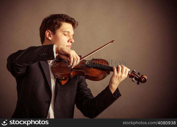 Art and artist. Young elegant man violinist fiddler playing violin on brown. Classical music. Studio shot.