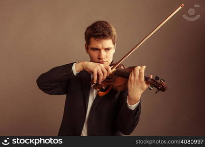 Art and artist. Young elegant man violinist fiddler playing violin on brown. Classical music. Studio shot.