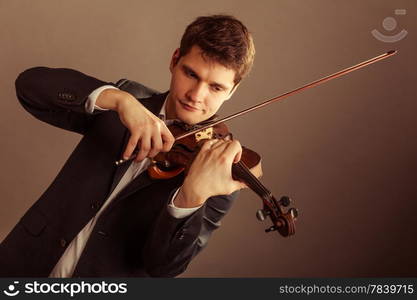 Art and artist. Young elegant man violinist fiddler playing violin on brown. Classical music. Studio shot.