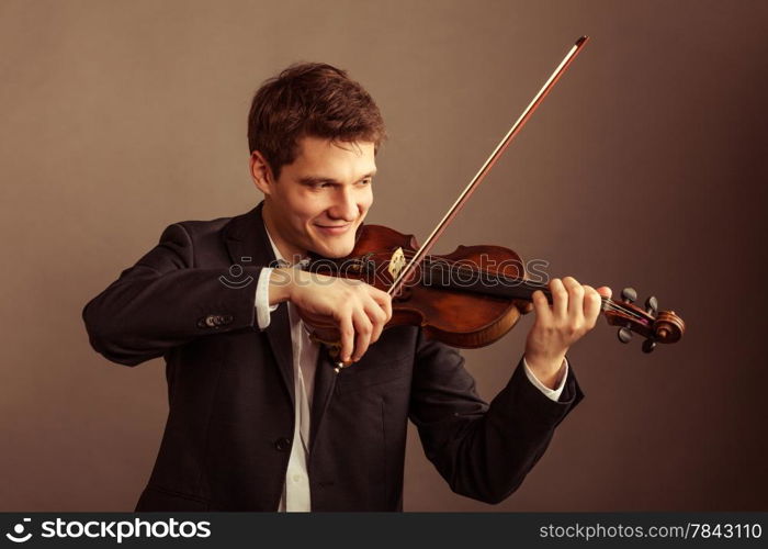 Art and artist. Young elegant man violinist fiddler playing violin on brown. Classical music. Studio shot.