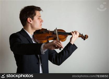 Art and artist. Young elegant man violinist fiddler playing violin on gray. Classical music. Studio shot.