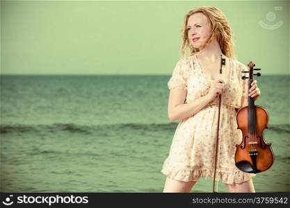 Art and artist. Young woman blond girl violinist fiddler holding violin and standing on the beach. Sea on the background. Classic music.