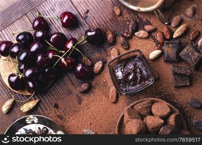art background with healthy delicious dark truffles, chocolate  and  ingridients   natural cocoa beans,  powder, chocolate, almonds  nuts and  ripe cherry. healthy sweets concept. flat lay