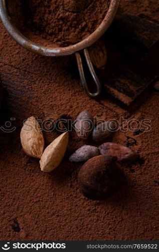 art background with healthy delicious dark truffles, chocolate  and  ingridients   natural cocoa beans,  powder, chocolate, almonds  nuts and  ripe cherry. healthy sweets concept. 