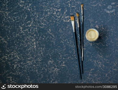 art brush and a jar on a golden blue background, top view. art brushes on a dark background