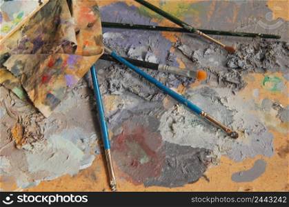 art brushes and a rag lying on a board with mixed colors. concept: artistic and creative chaos. art craft, paints