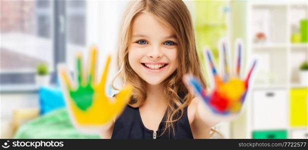 art, creativity and painting concept - happy smiling little girl showing painted hands over home room background. smiling girl showing painted hands at home