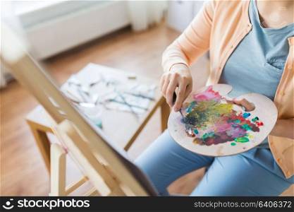 art, creativity and people concept - artist woman with palette knife and easel painting at studio. artist with palette knife painting at art studio