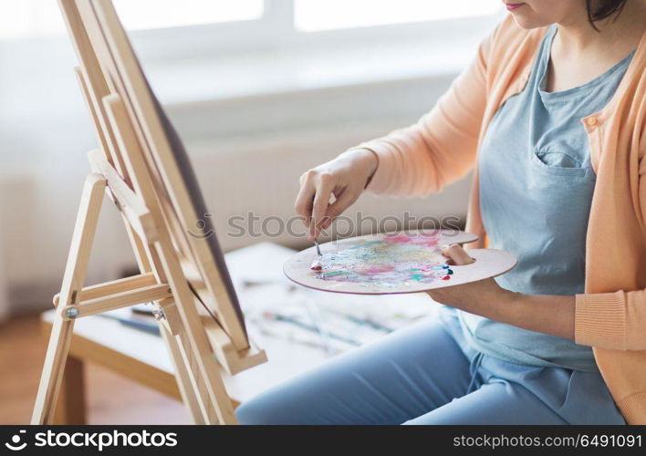 art, creativity and people concept - artist woman with palette knife and easel painting at studio. artist with palette knife painting at art studio. artist with palette knife painting at art studio