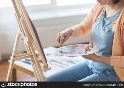 art, creativity and people concept - artist woman with palette knife and easel painting at studio. artist with palette knife painting at art studio. artist with palette knife painting at art studio