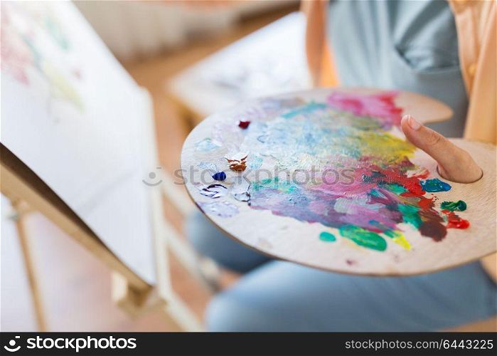 art, creativity and people concept - close up of artist with paint on palette painting at studio. artist with paint palette painting at art studio