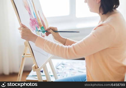 art, creativity and people concept - close up of artist with paint brush and easel painting still life on paper at studio. artist with brush painting still life at studio