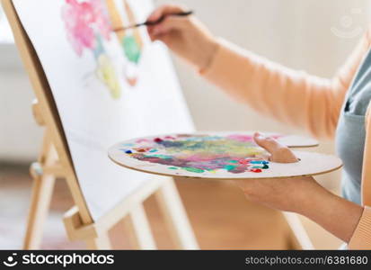 art, creativity and people concept - close up of artist with palette, brush and easel painting at studio. artist with palette and brush painting at studio