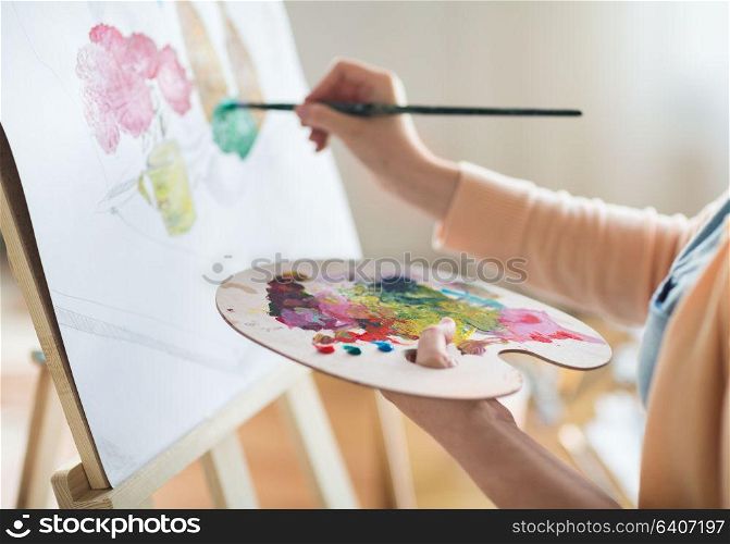 art, creativity and people concept - close up of artist with palette and brush painting still life on paper at studio. artist with palette painting at art studio