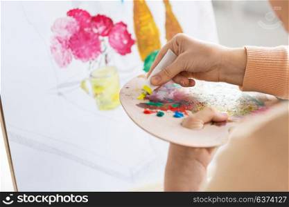 art, creativity and people concept - close up of artist woman applying paint to palette and painting still life on easel at studio. artist applying paint to palette at art studio