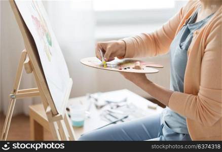 art, creativity and people concept - close up of artist woman applying paint to palette and painting still life on easel at studio. artist applying paint to palette at art studio
