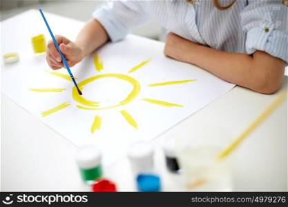 art, creativity, people and childhood concept - girl with brush drawing sun on paper. girl with brush drawing sun on paper