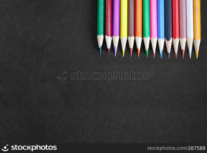 Art drawing banner poster concept, Colorful crayon pencils in a row on top right corner on black canvas with textured background with copy space. View from above. Closeup.