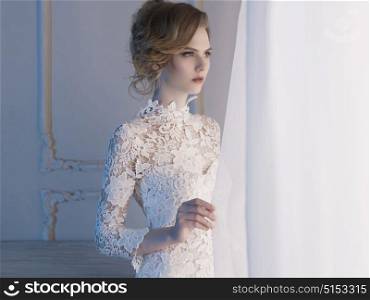 Art fashion portrait of beautiful gorgeous woman in lace dress at the window. Beauty and health. Wedding style. Bridal morning