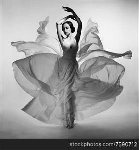 Art fashion studio photo of beautiful elegant woman in blowing dress. Flying dress. Freedom concept. Fashion style of flowing dress